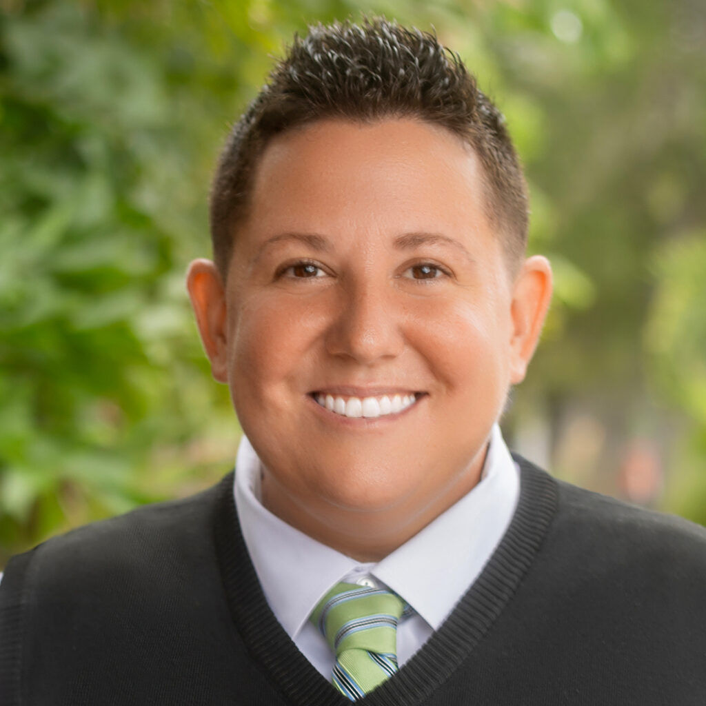 Callen Jones, a board member of TransNetwork, standing outdoors with hands in pockets, wearing a black vest, white shirt, and green striped tie.