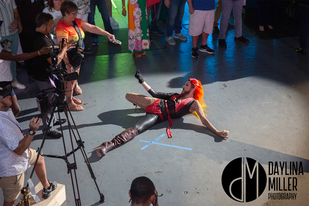 Lilith performing a dramatic dance move, death drop, on the floor, surrounded by an engaged audience at the UNI-Tea Dance.